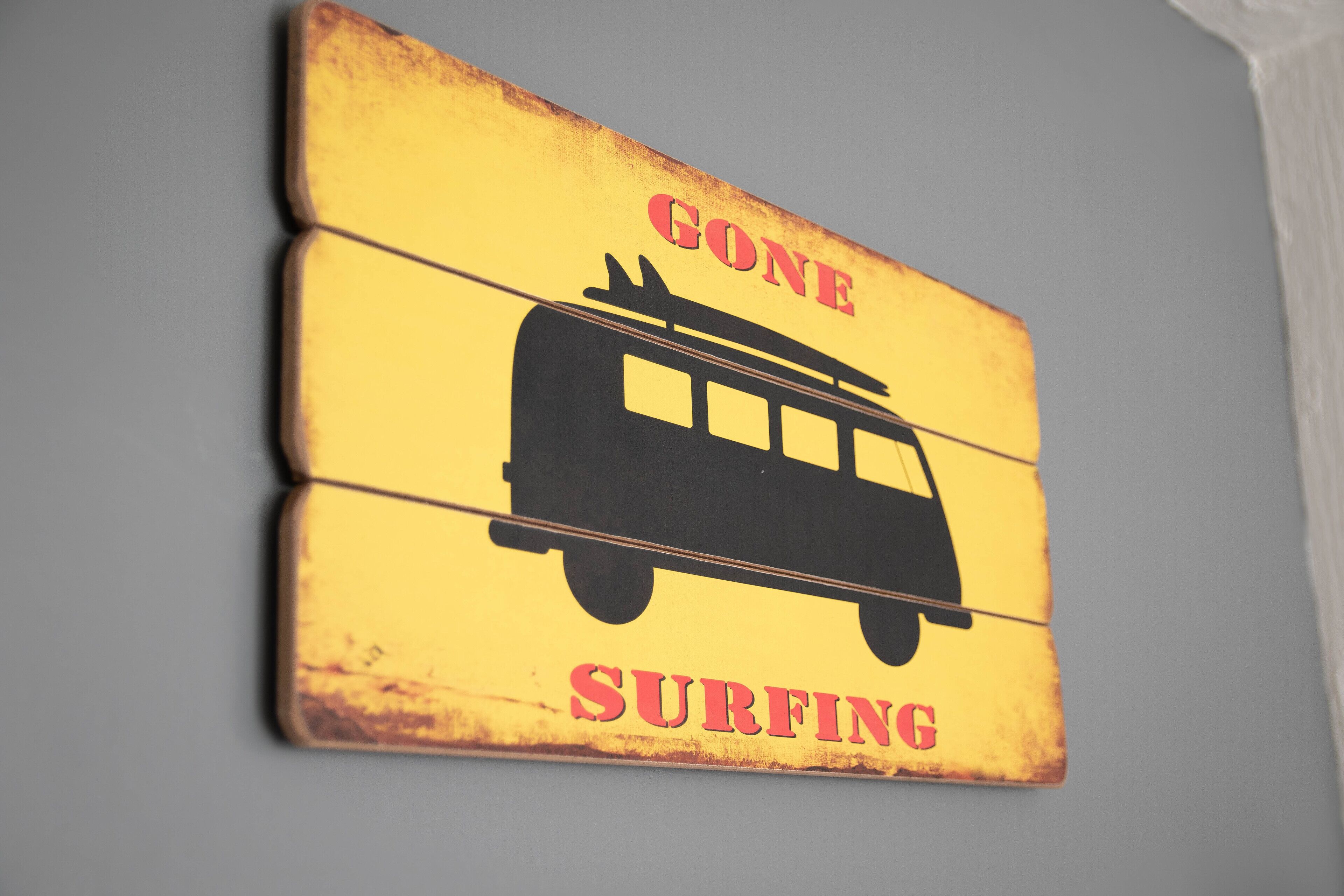Een geel bord met een silhouet van een bus en de tekst 'GONE SURFING'.