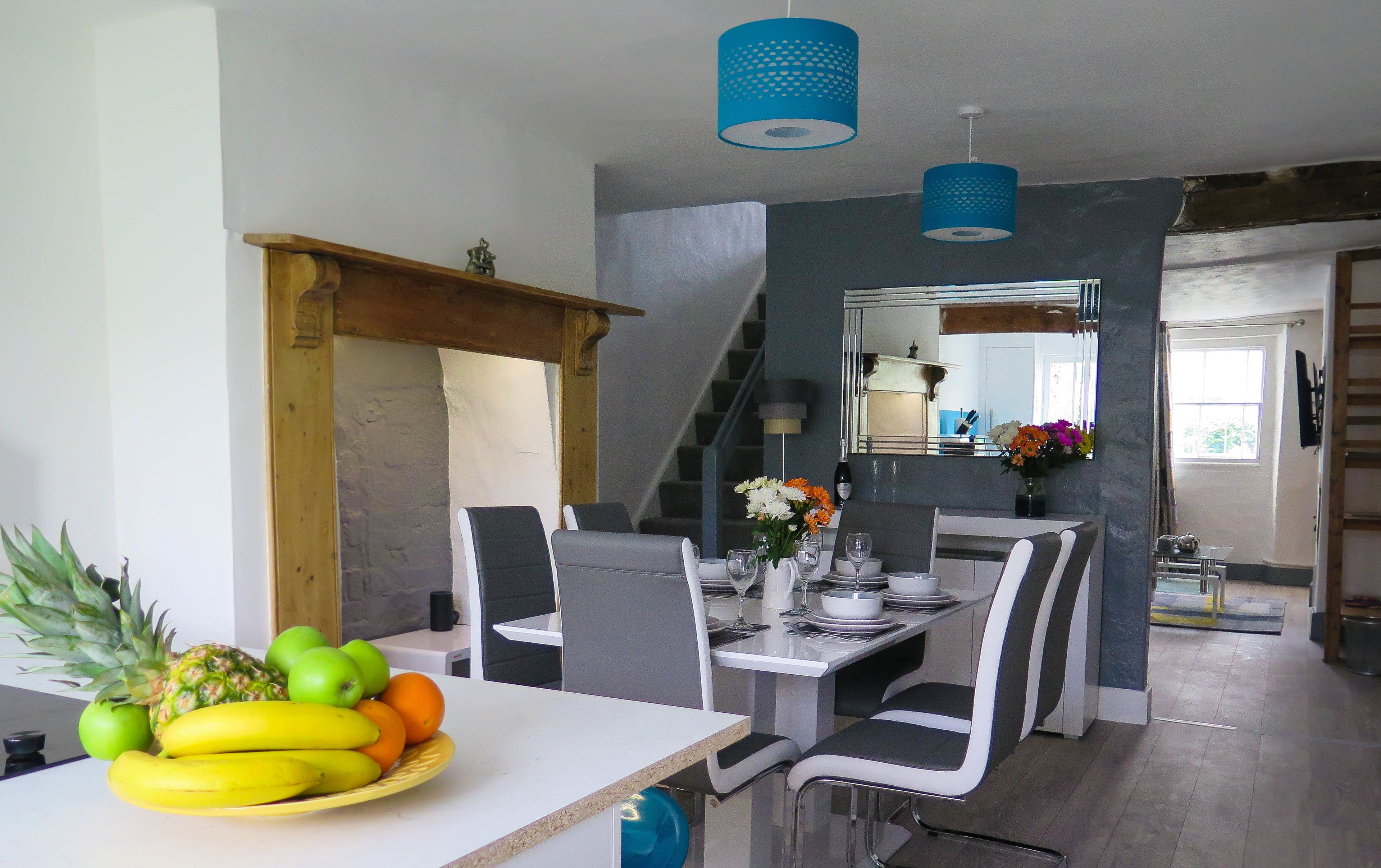 A dining area with a table set for four, chairs, a fruit bowl, and a staircase leading to another level.
