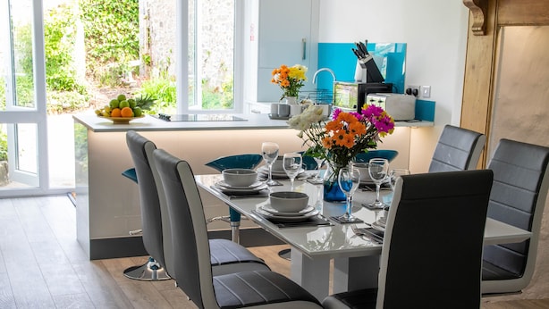 A modern dining area with a glass table, black chairs, and a vase of flowers. - Westeria Cottage (Barnstaple)