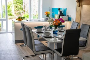 A modern dining area with a glass table, black chairs, and a vase of flowers. - Westeria Cottage (Barnstaple)