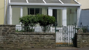 A two-story house with a white exterior, a front porch with a glass door, and a stone wall in front. - Westeria Cottage (Barnstaple)