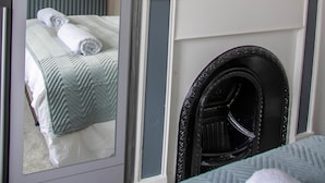 A bedroom with a bed, a mirror, a fireplace, and a painting of glasses. - Westeria Cottage (Barnstaple)