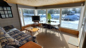 Une pièce chaleureuse avec un canapé, une petite table, un téléviseur posé sur un meuble et une vue sur un paysage enneigé par de grandes fenêtres.