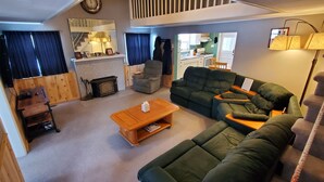 Un salon chaleureux avec une cheminée, des canapés verts, une table basse en bois et un escalier menant à un niveau supérieur.