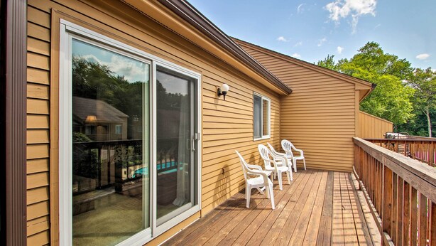 Une terrasse avec un plancher en bois et des chaises en plastique blanches, une porte-fenêtre coulissante et une petite fenêtre sur une maison de couleur beige.