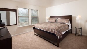 Un dormitorio con cama, cómoda, mesita de noche, lámpara y ventana con persianas.