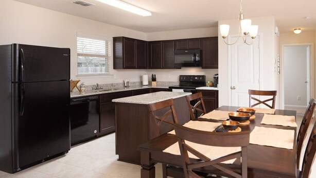 Una cocina moderna con armarios de madera oscura, un refrigerador negro, un microondas y un comedor con mesa y sillas.