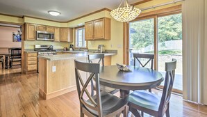 A kitchen with wooden cabinets, a microwave, a stove, and a dining area with a table and chairs. - Walk to Buzzards Bay Beach: Spacious Onset Home (Onset)