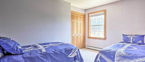 A bedroom with two beds, a window, and a wooden door.