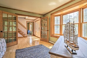 A spacious room with a wooden staircase, large windows, and a model ship on a table. - Walk to Buzzards Bay Beach: Spacious Onset Home (Onset)