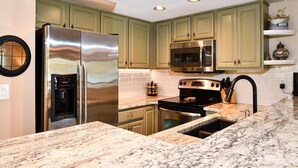 A kitchen with green cabinets, stainless steel appliances, a marble countertop, and under-cabinet lighting. - Aldea A8 Beachfront 2 Bedroom 2 Bath - Tranquil Belleair Beach (Belleair Beach)