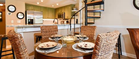 A dining area with a round table, wicker chairs, and a spiral staircase in the background.