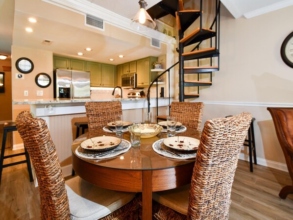 A dining area with a round table, wicker chairs, and a spiral staircase in the background. - Aldea A8 Beachfront 2 Bedroom 2 Bath - Tranquil Belleair Beach (Belleair Beach)