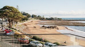A coastal road with parked cars, a sandy beach, and a view of the sea.