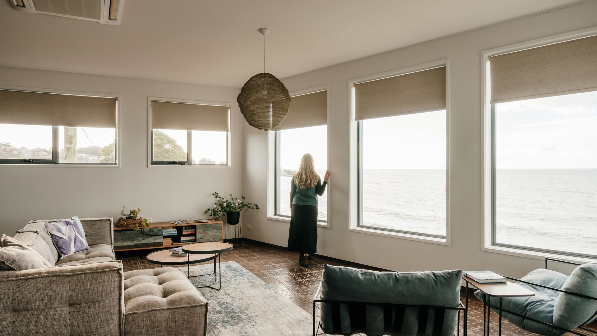 A spacious living room with large windows overlooking the sea, a cozy seating area, and a modern pendant light.
