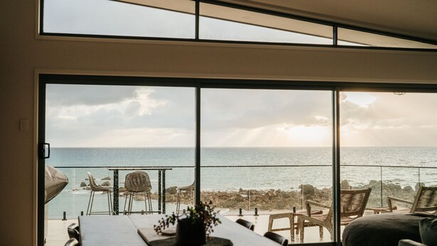 A room with a large sliding glass door leading to a balcony overlooking a beach. - Absolute waterfront beauty in Tasmania (Penguin)