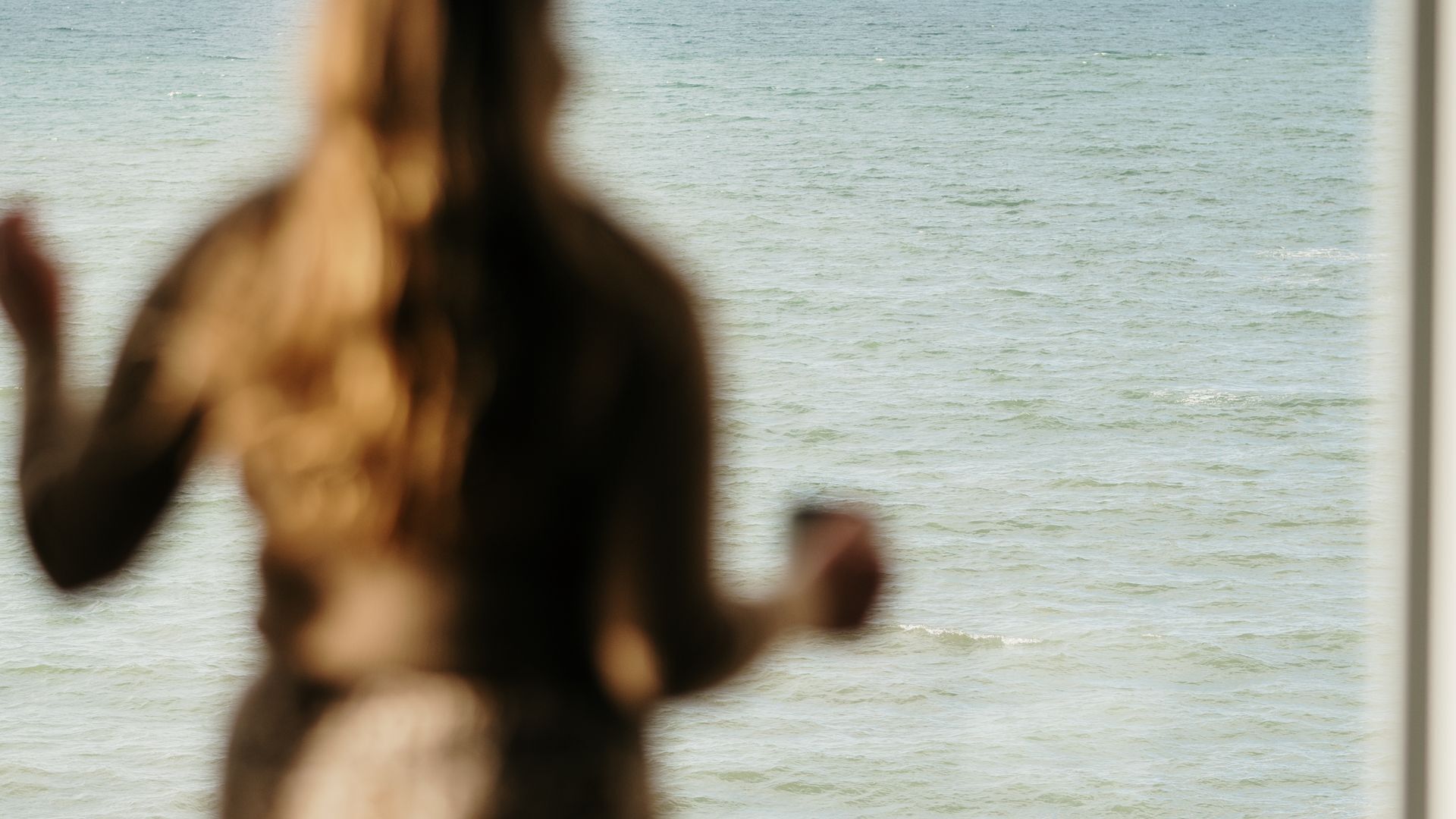 A blurred figure in motion, with a view of a calm sea in the background.