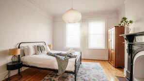 A bedroom with a bed, bedside lamp, wooden floor, windows, and a fireplace.