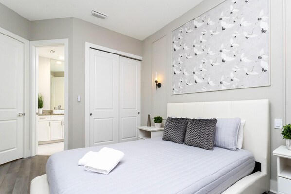 A bedroom with a large bed, white walls, a decorative wall piece, and a door leading to a bathroom.