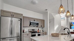 A modern kitchen with stainless steel appliances, a central island, and pendant lighting. - Fantastic house next to Disney. Enjoy private heated pool! (Kissimmee)
