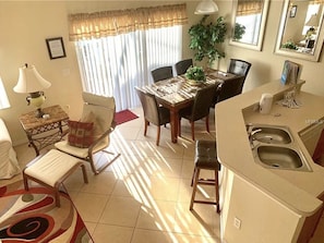 Cozy living space with a dining area and kitchenette, featuring a dining table, chairs, and a potted plant.