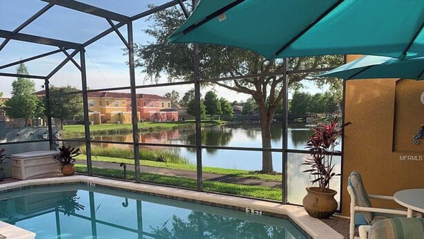 A swimming pool with a glass enclosure, a view of a lake, and outdoor seating. - Fantastic house next to Disney. Enjoy private heated pool! (Kissimmee)