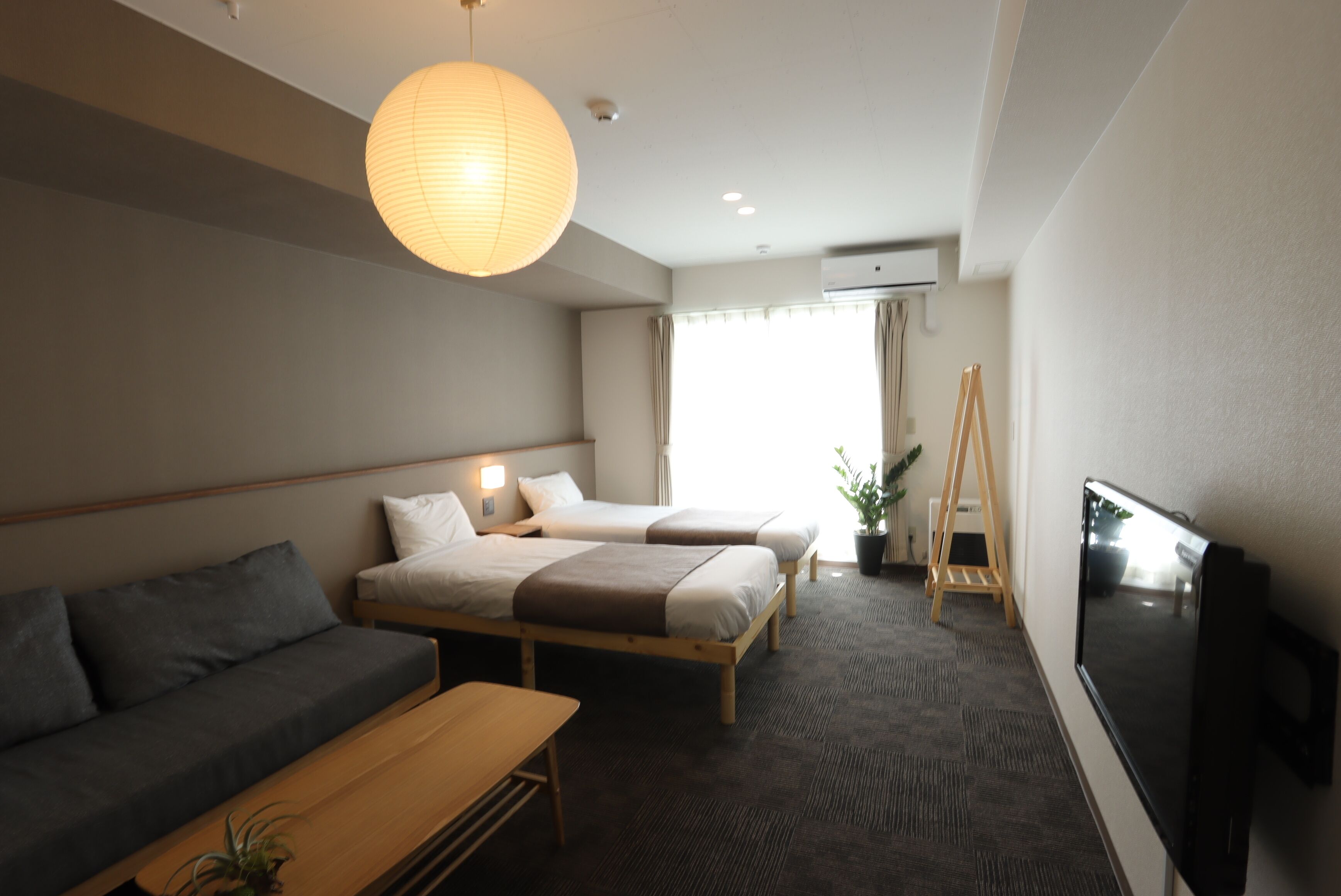 A hotel room with two beds, a sofa, a TV, and a large window.