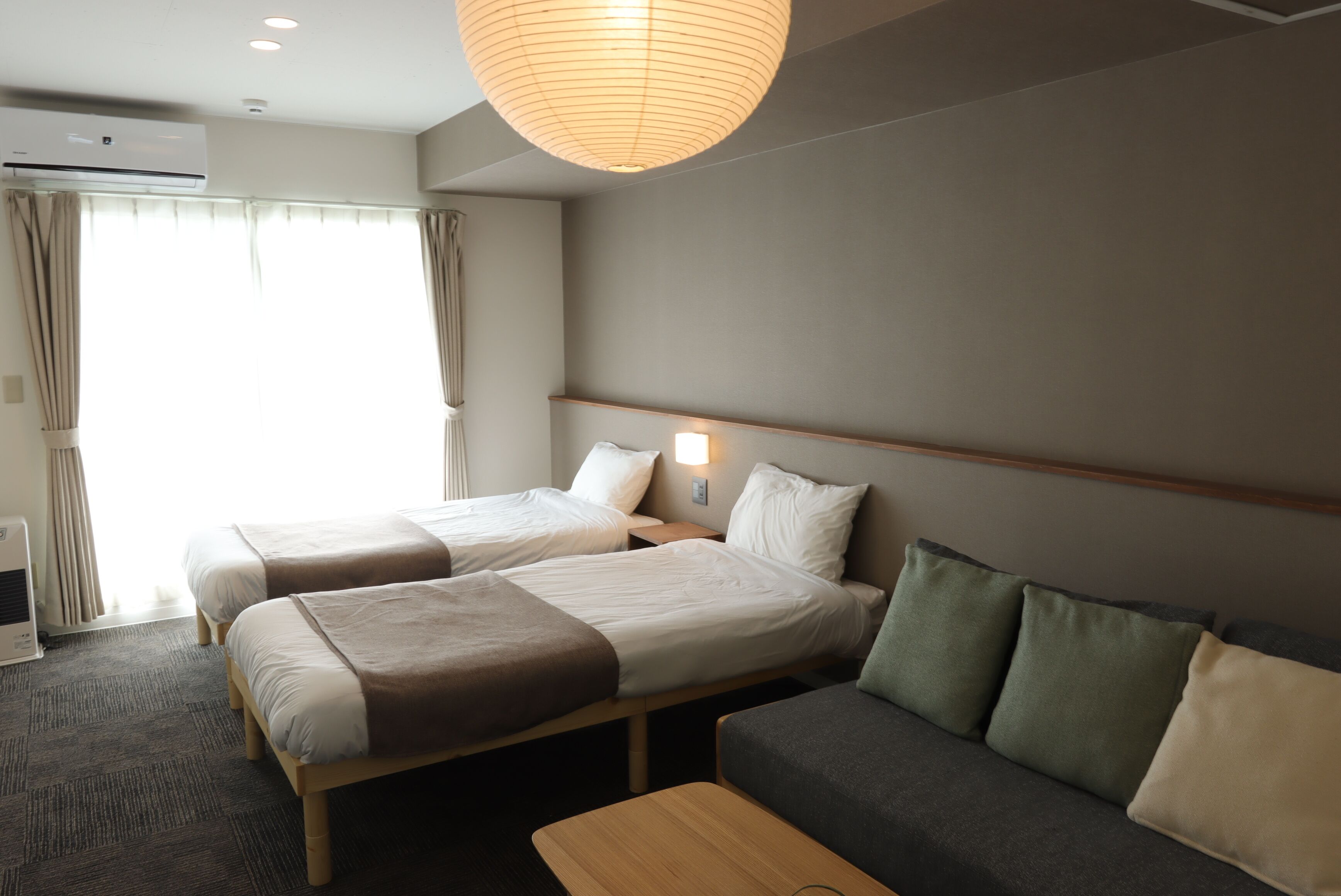 A hotel room with two beds, a sofa, a wooden coffee table, and a ceiling light.