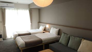 A hotel room with two beds, a sofa, a wooden coffee table, and a ceiling light.