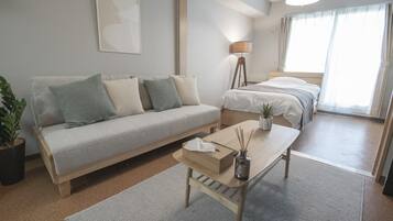 A modern hotel room with a sofa, a small table with a vase, a lamp, and a bed.