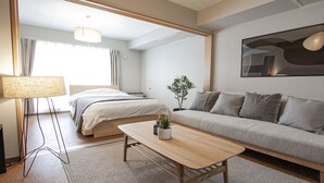A modern hotel room with a bed, a sofa, a coffee table, a lamp, and a potted plant. - UCHI Living Stay Otaru Suitengu (Otaru)