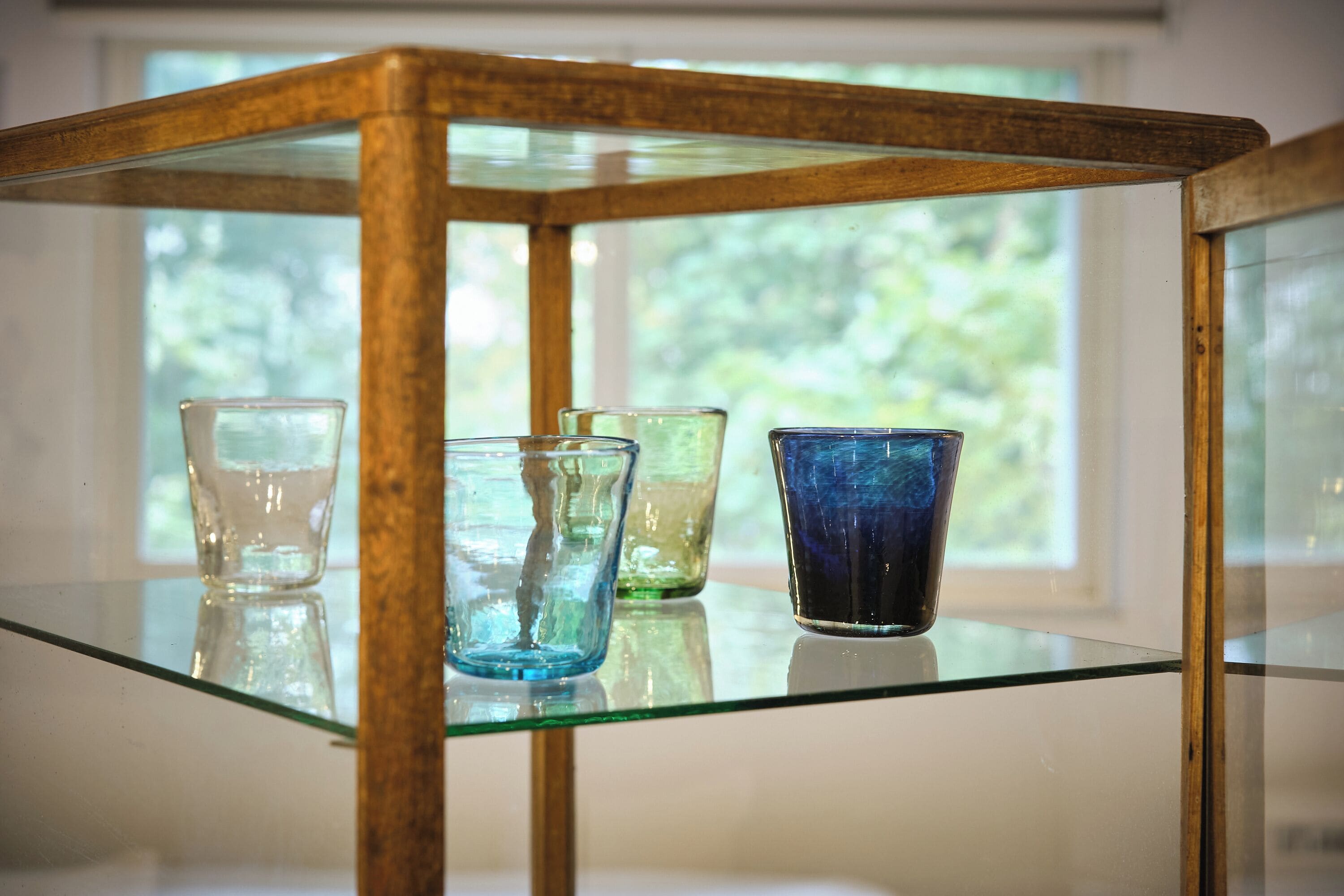 A glass shelf with four colored glass vases.