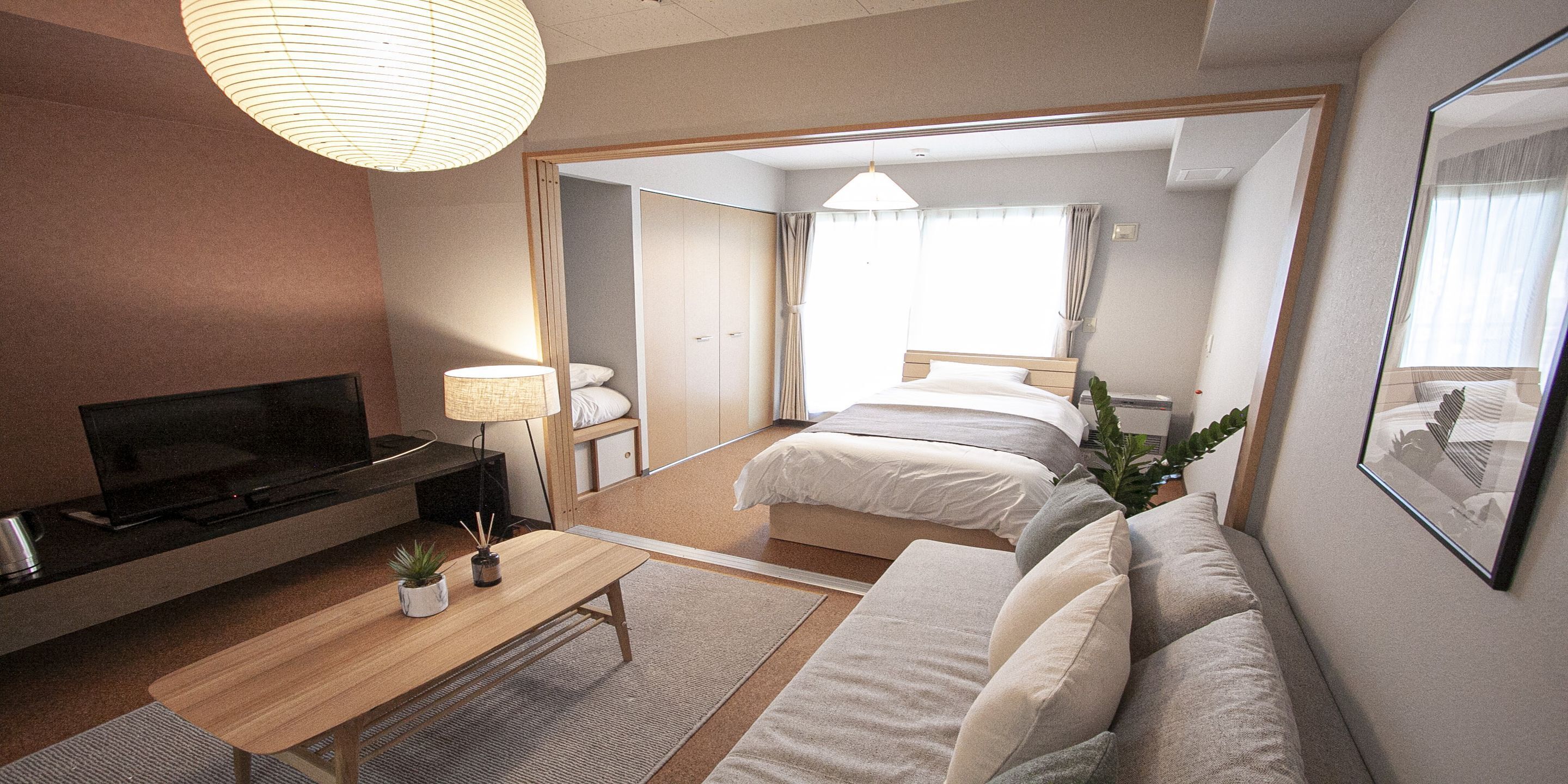 A hotel room with a TV, a bedside table with a lamp, a sofa, and a bed.