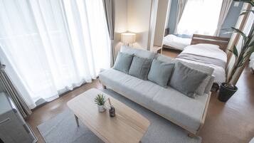 A hotel room with a grey sofa, a wooden coffee table, a small potted plant, and a lamp.