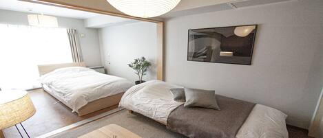 A modern hotel room with two beds, a small table, a potted plant, and a large abstract painting on the wall.