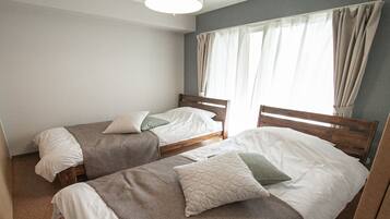 A room with two single beds, a window with curtains, and a plain wall.