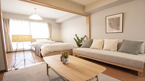 A hotel room with a bed, a sofa, a small table with a plant, a lamp, and a framed picture on the wall. - UCHI Living Stay Otaru Suitengu (Otaru)