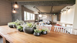 A modern interior with a wooden reception desk, potted plants, and a seating area with a white railing. - UCHI Living Stay Otaru Suitengu (Otaru)