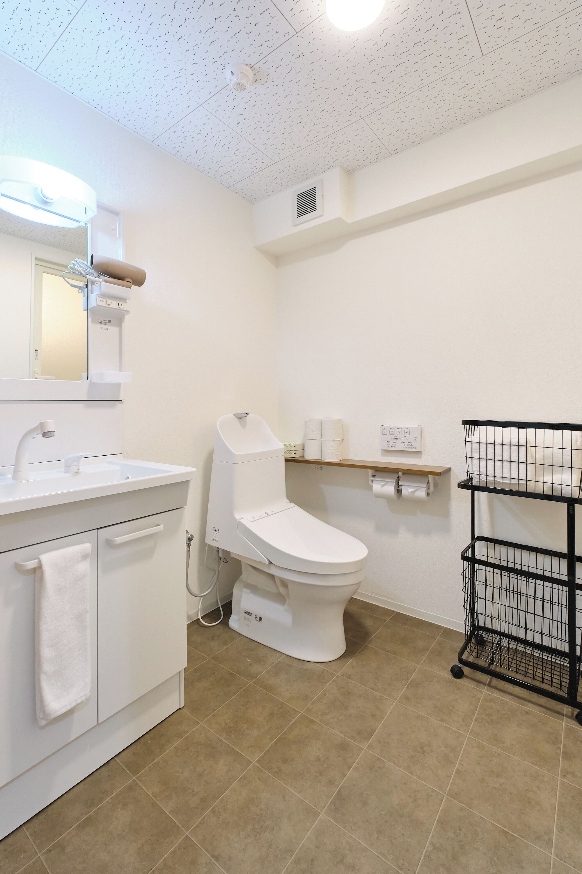 Un baño con lavamanos blanco, espejo, inodoro y repisa metálica negra.