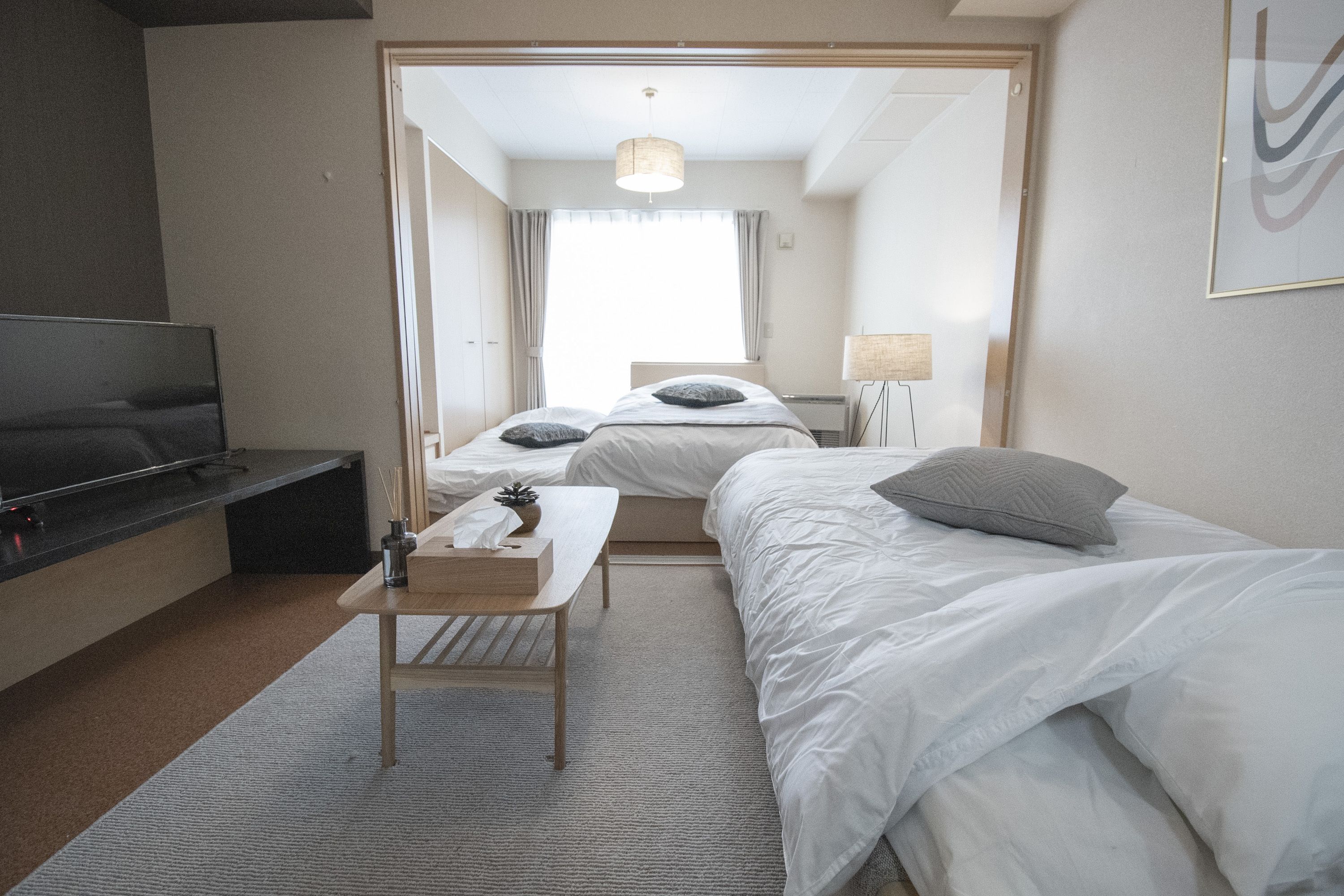 Ein Hotelzimmer mit Fernseher, zwei Betten, einem kleinen Tisch und einer Lampe.