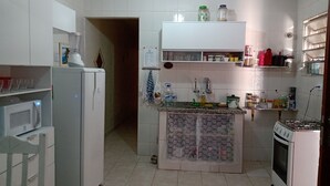Una cocina compacta con armarios blancos, un refrigerador, un microondas, una estufa y una pequeña isla con un lavamanos. Hay estantes sobre la isla que sostienen frascos y algunos utensilios de cocina.