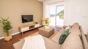 A living room with a flat-screen TV, a yellow armchair, a beige sofa, and a large window with a view of the sea. - Casa do Outeiro in a rural area (Povoação)