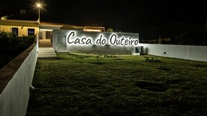 A nighttime view of a house named "Casa do Outeiro" with a well-lit entrance and a grassy lawn. - Casa do Outeiro in a rural area (Povoação)