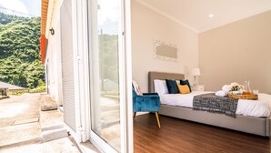 A bedroom with a bed, a nightstand, a lamp, and a view of a green landscape through a sliding door. - Casa do Outeiro in a rural area (Povoação)