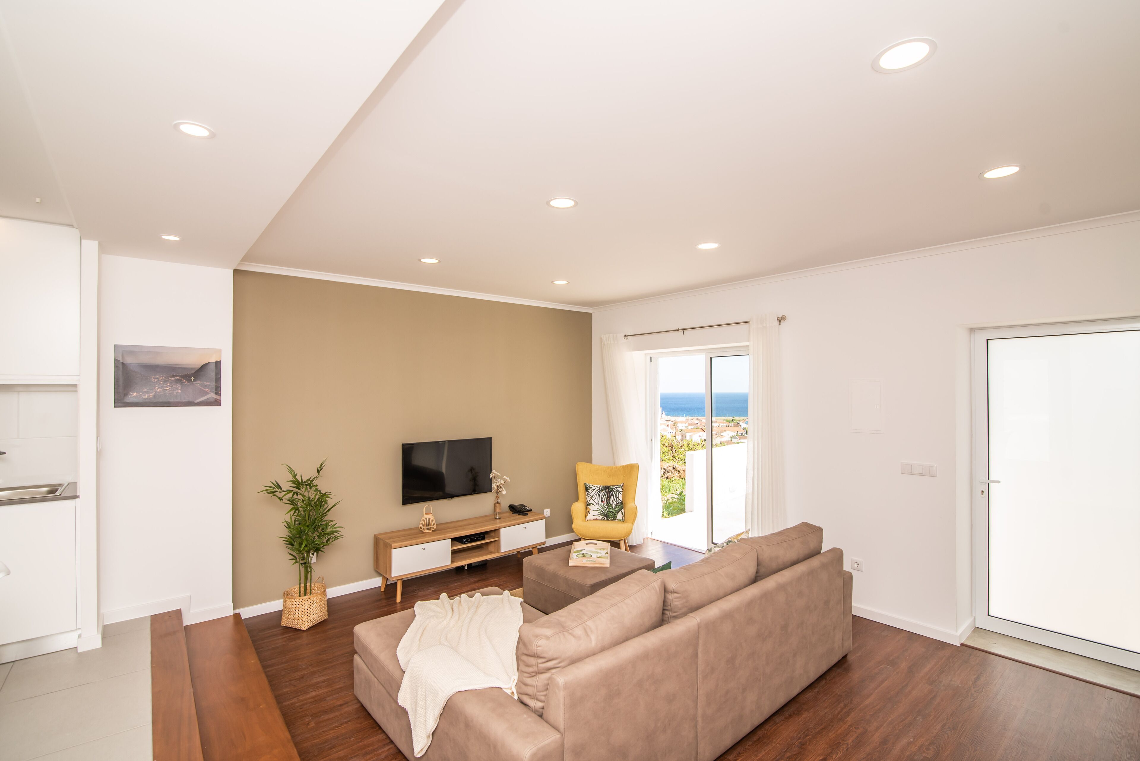 A modern living room with a sofa, a flat-screen TV, a wooden cabinet, and a large window with a view.
