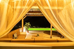 Uma área de estar aconchegante ao ar livre, com vista para um campo esportivo iluminado à noite.
