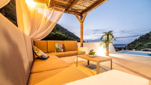 A cozy outdoor seating area with a sofa and a table, overlooking a pool and a mountainous landscape. - Casa do Outeiro in a rural area (Povoação)