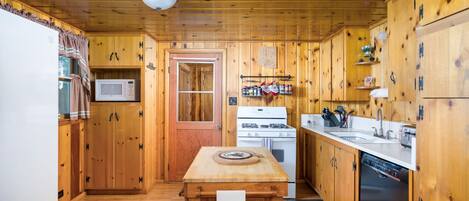 A cabin-style kitchen with wooden walls, a microwave, a stove, and a sink.