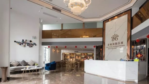 Un hall d’hôtel moderne avec un comptoir d’accueil, un espace salon et un lustre.