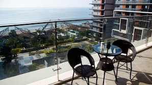 Un balcon doté d’une balustrade en verre donnant sur une piscine et des immeubles, ainsi que deux chaises et une petite table.